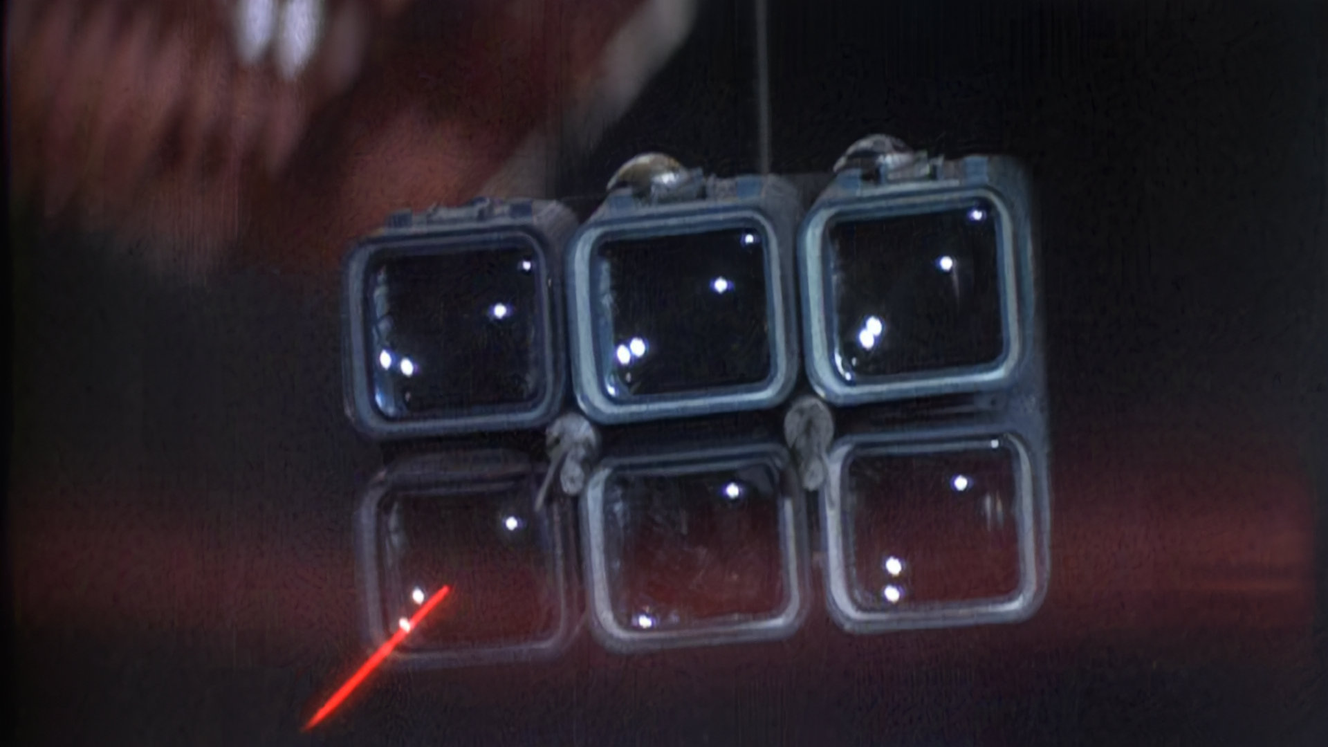 Star Wars still of a red laserbeam about to hit a cluster of six square glass lights, possibly a security camera