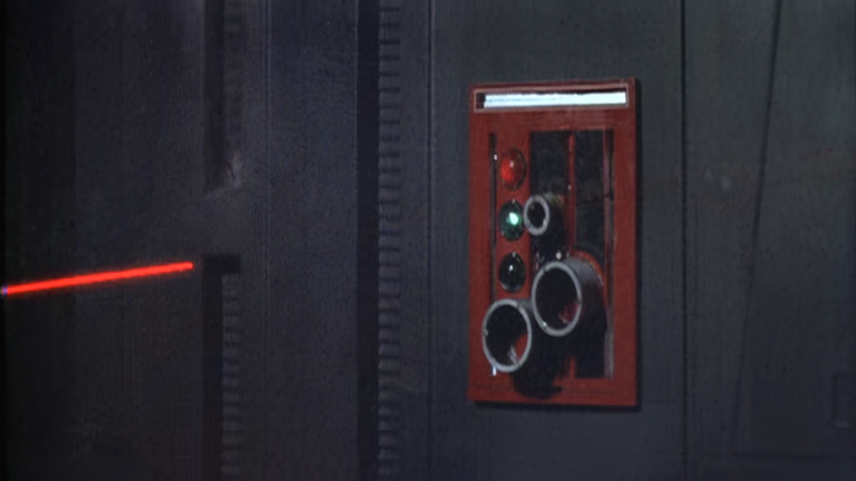 Star Wars still of a red laserbeam about to hit a red, fire-alarm type wall fixture